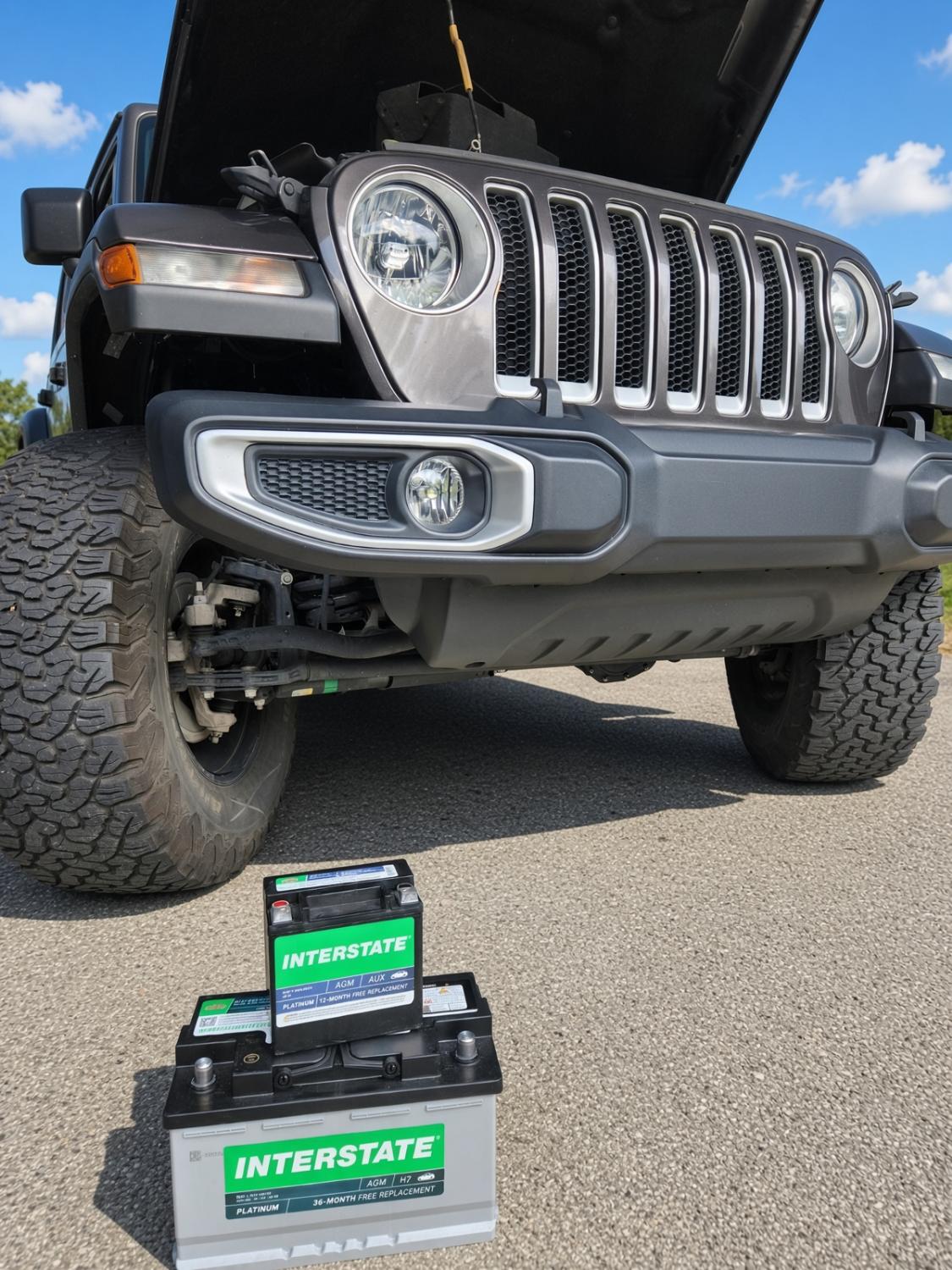 At-home car battery replacement on a gray Jeep in the DMV, hood open with new batteries.