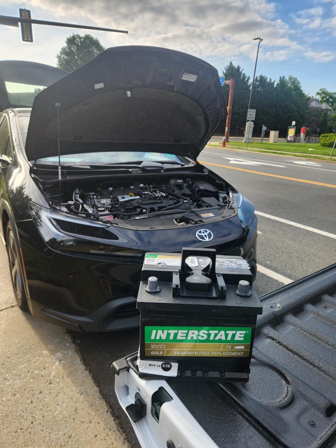 Black Toyota with the hood open and a small auxiliary battery.