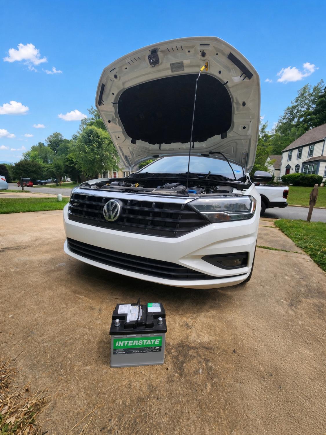 White Volkswagen with the hood open and a new battery on the driveway.